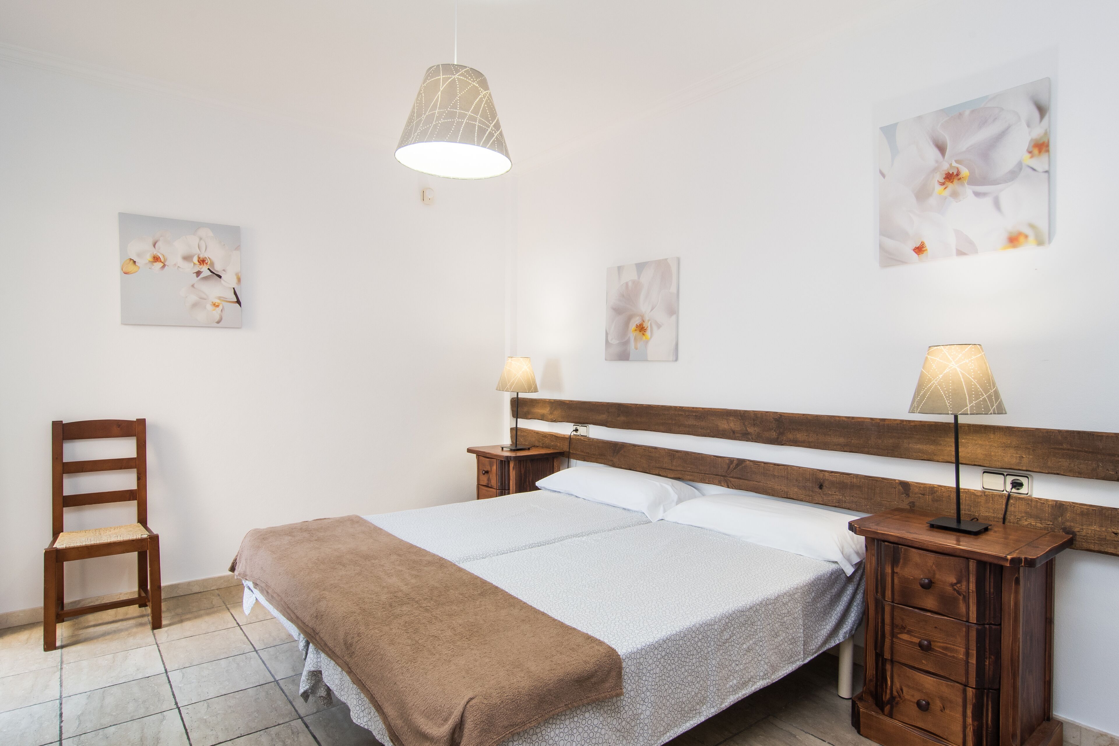 Une chambre bien rangée, avec un lit en bois, une chaise et deux lampes fixées au mur.