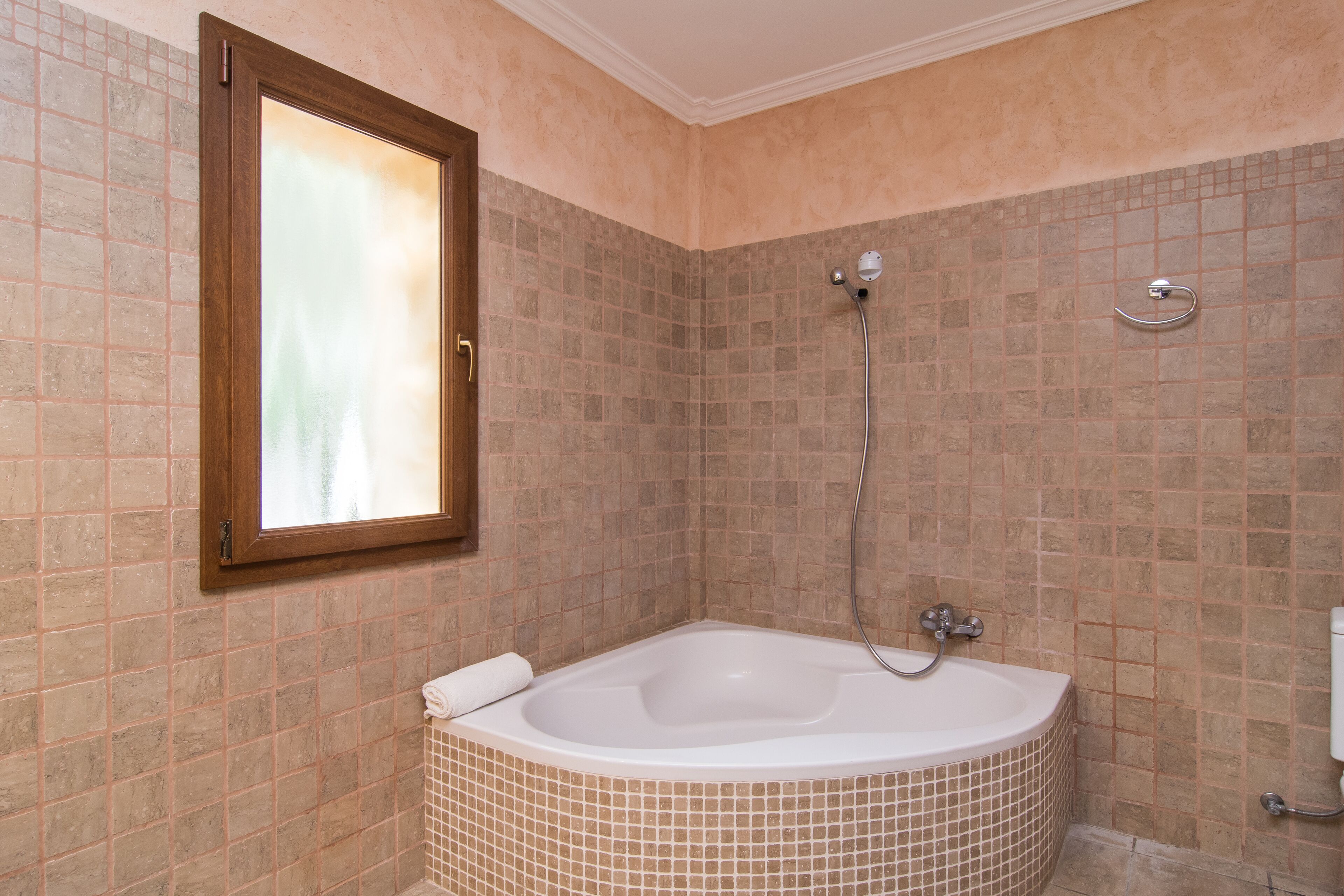 A bathroom with a large bathtub, a shower, and a window with a wooden frame.