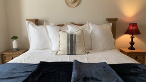 Un letto ben rifatto con lenzuola bianche, numerosi cuscini, una lampada da comodino e una piccola pianta su un comodino in legno.