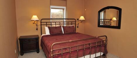 A bedroom with a metal bed frame, two bedside tables with lamps, a window, and a mirror on the wall.