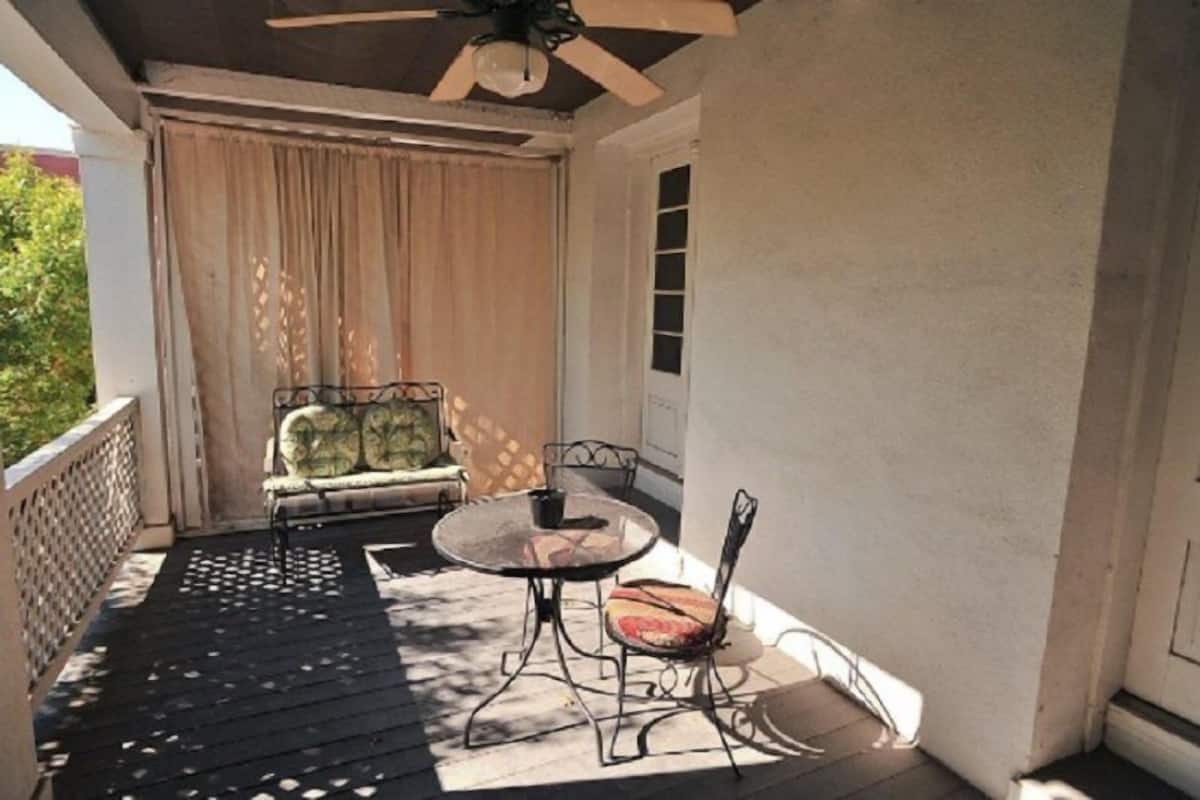 A covered outdoor seating area with a table and chairs, a cushioned bench, and a ceiling fan.
