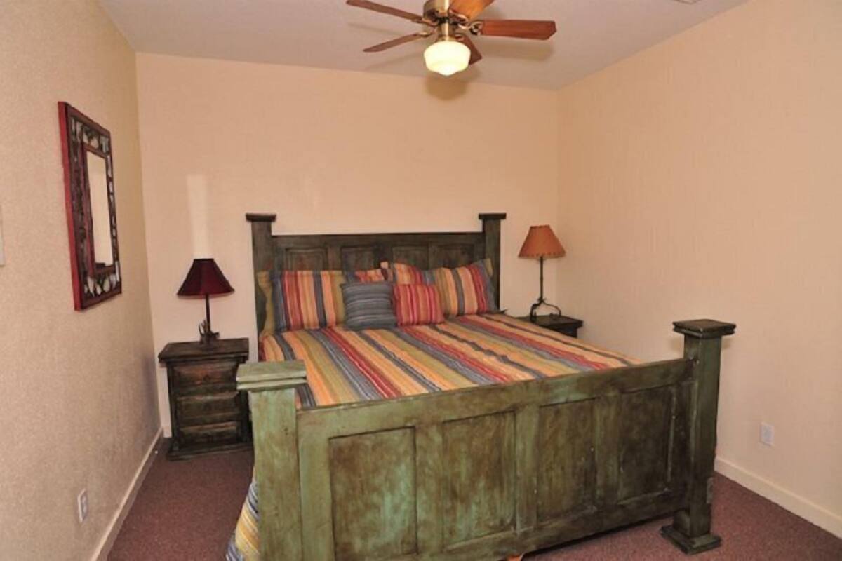 A bedroom with a wooden bed, a ceiling fan, a nightstand with a lamp, and a framed picture on the wall.