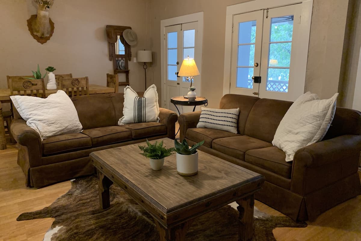 A cozy living room with a brown sofa set, a wooden coffee table with plants, a lamp, and a rustic wall decor.