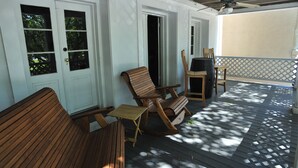 Un portico coperto con mobili in legno, tra cui una poltrona a dondolo e una panca, e un barbecue.