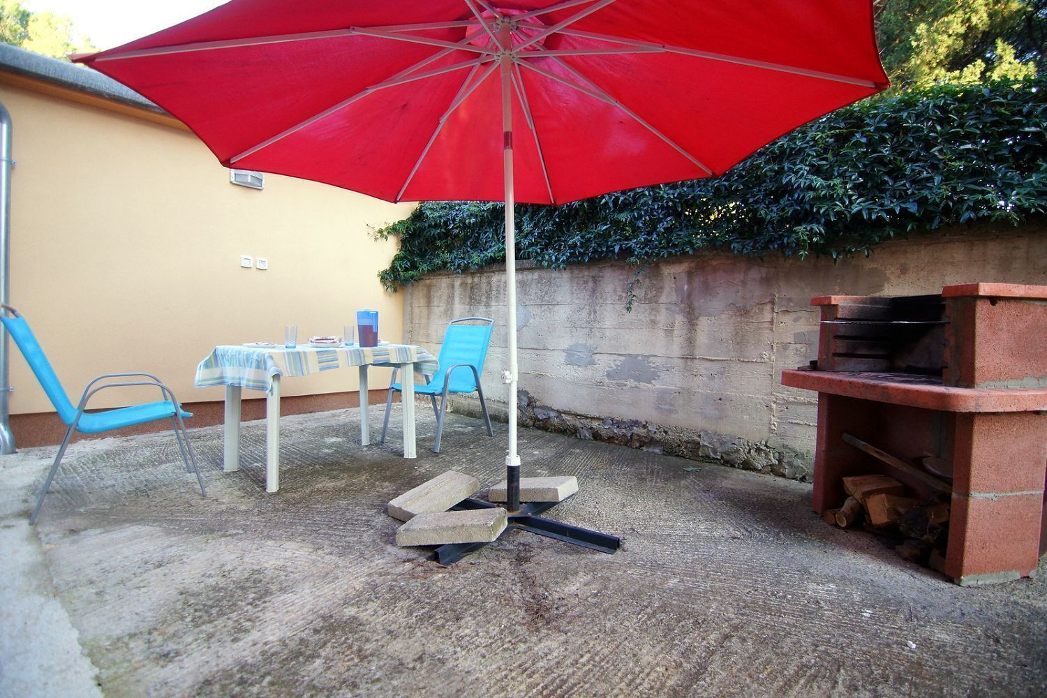 Terrassa exterior amb una paraigua vermella, taula amb caires i una barbacoa.