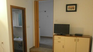 Ein Zimmer mit einem Holzschrank, einem Fernseher darauf und einem durch eine offene Tür einsehbaren Badezimmer.