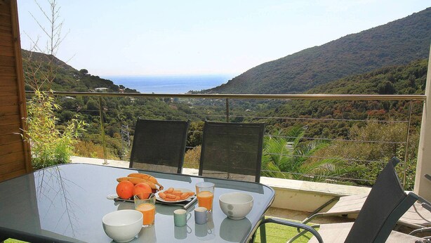A table with a glass top, surrounded by chairs, overlooking a scenic view of hills and the sea. - Uribellinu 2, nice T3 mountain sea view (santa maria di lota)