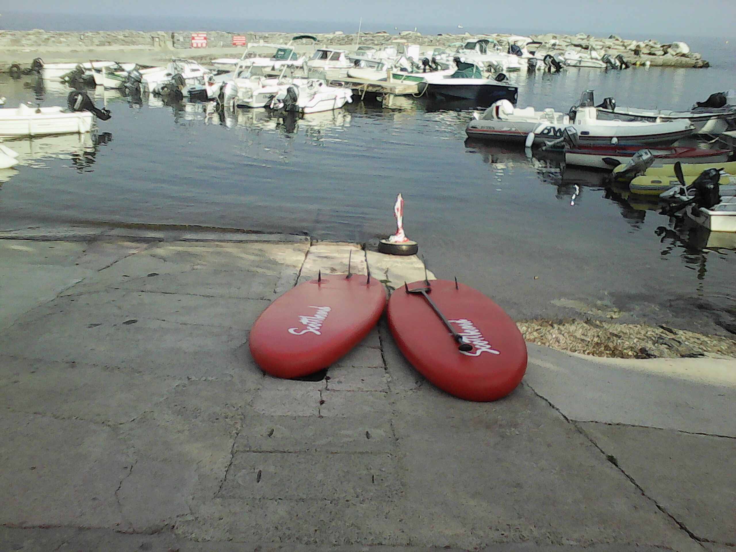 Un puerto deportivo con barcos amarrados y dos tablas de remo rojas en el muelle.