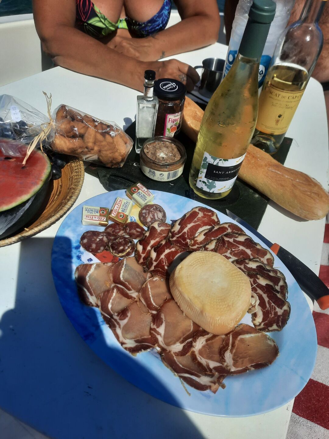 A table with a plate of cured meats, a bottle of wine, and a loaf of bread.