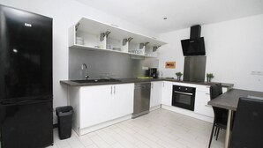 A modern kitchen with white cabinets, a black refrigerator, stainless steel appliances, and a dining area with a table and chairs. - Uribellinu 2, nice T3 mountain sea view (santa maria di lota)