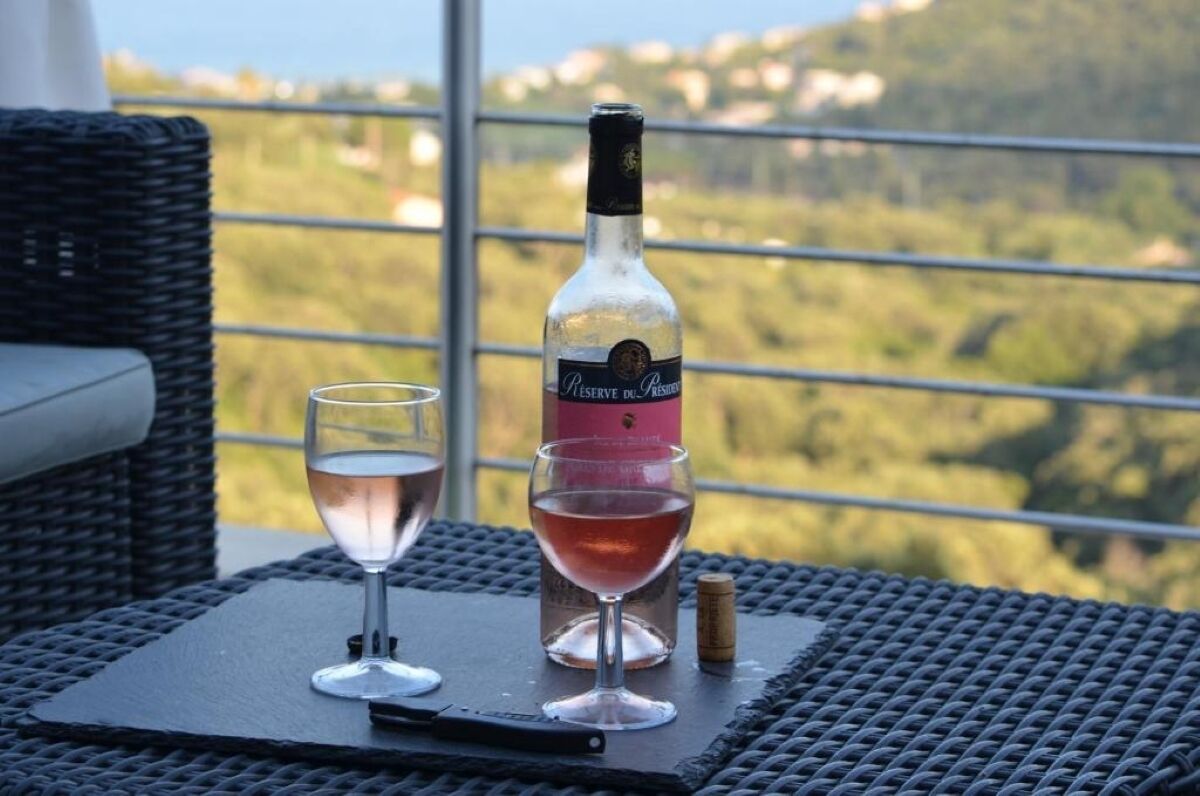 A bottle of wine and two glasses on a table with a view of a green landscape.