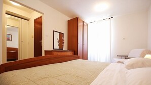 A hotel room with a large bed, a wardrobe, a desk with a chair, and a window with curtains. - Apartment with pool, air conditioning, WiFi (Krnica)