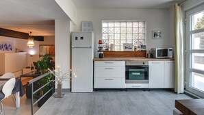 Et moderne køkken med hvide skabe, en indbygget ovn, en mikroovn og et vindue med matteret glas.