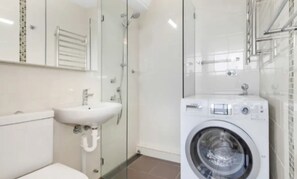 A modern bathroom with a glass shower enclosure, a built-in sink, and a front-loading washing machine. - Beachside Paradise - Ocean Views, Central Position (Manly)