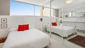 A modern bedroom with a large bed, a dresser, and a mirror. - Beachside Paradise - Ocean Views, Central Position (Manly)