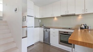A modern kitchen with white cabinets, a stainless steel dishwasher, and a wooden countertop. - Beachside Paradise - Ocean Views, Central Position (Manly)
