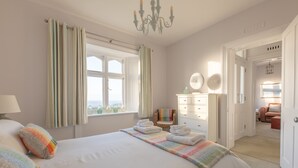 A hotel room with a large bed, a chair, a dresser, and a view of the outside. - Gurnard Cottage, St Catherine's Lighthouse in Niton, the Isle of Wight. (Undercliffe)