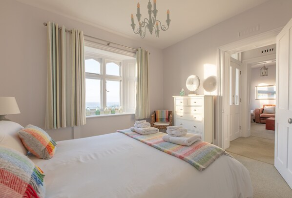 A hotel room with a large bed, a chair, a dresser, and a view of the outside.