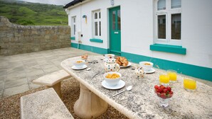 A breakfast table set with eggs, croissants, bowls of cereal, and glasses of orange juice outside a building with a green door and white walls. - Gurnard Cottage, St Catherine's Lighthouse in Niton, the Isle of Wight. (Undercliffe)
