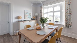 A dining area with a wooden table, yellow chairs, a vase with flowers, and a window with curtains. - Gurnard Cottage, St Catherine's Lighthouse in Niton, the Isle of Wight. (Undercliffe)