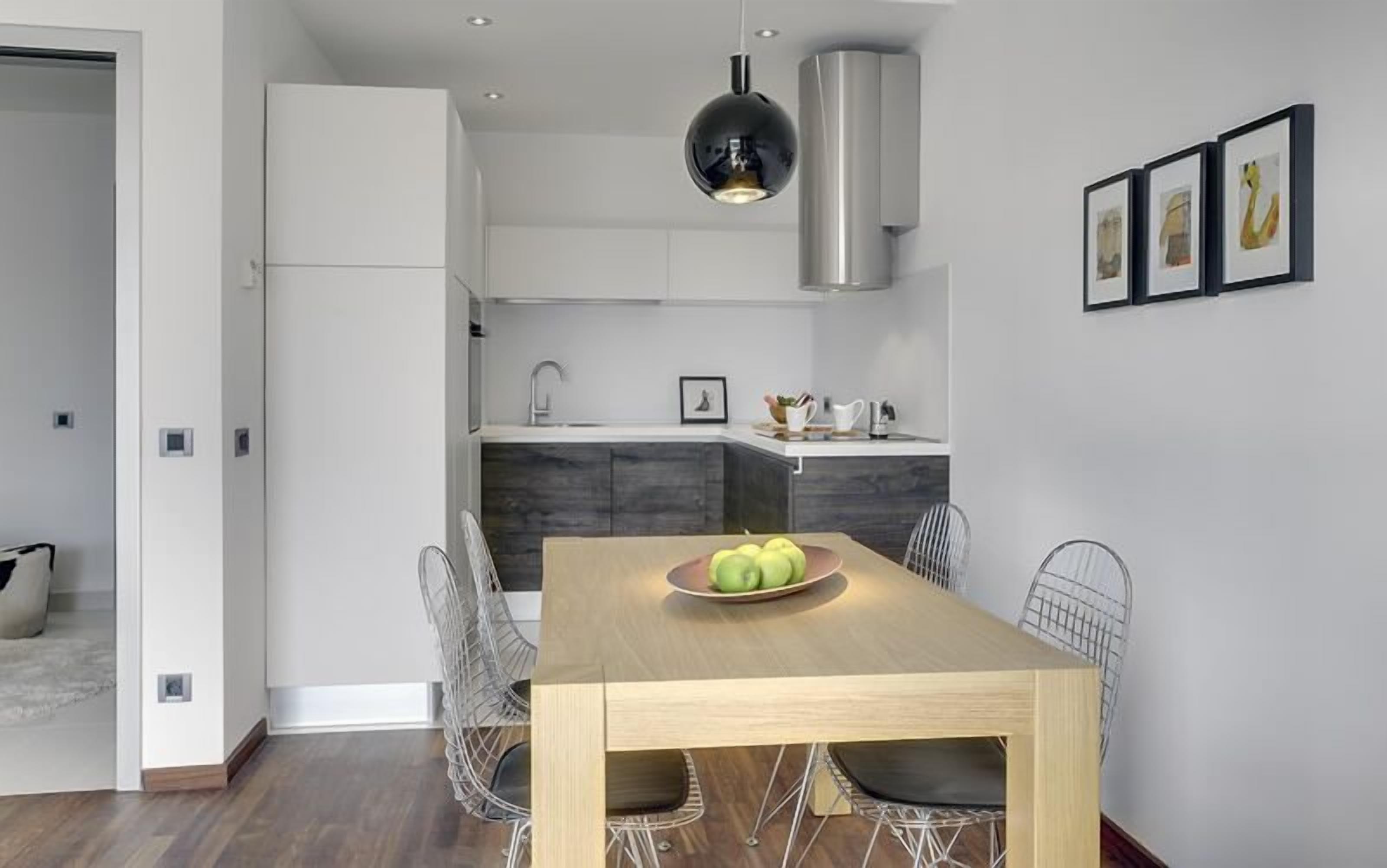 A modern kitchen with white cabinets, a stainless steel range hood, and a dining area with a wooden table and wire chairs.