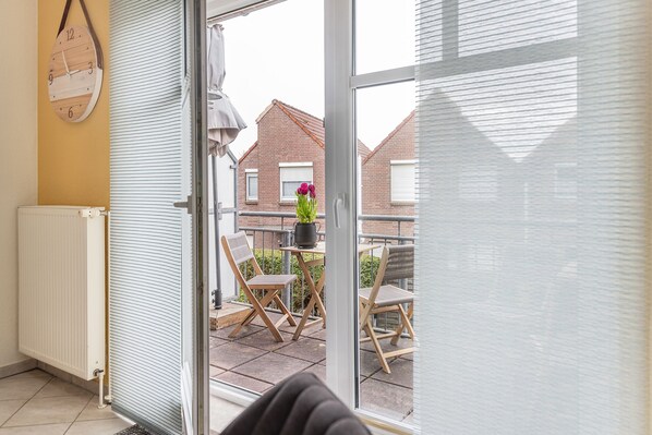 Un balcon avec une porte-fenêtre coulissante, un radiateur blanc et deux chaises en bois, agrémenté d’une plante en pot.