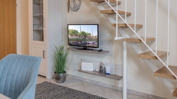 A modern living room with a flat-screen TV, a wooden staircase, a potted plant, and a built-in cabinet. - High-quality and bright: The upstairs apartment offers the fine and sat (Carolinensiel)
