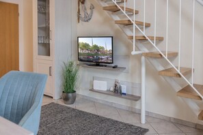 Un salon moderne doté d’un t éléviseur à écran plat, d’un escalier en bois, d’une plante en pot et d’une bibliothèque intégrée.