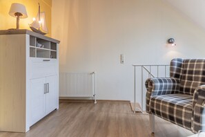 Une pièce avec un meuble blanc, un fauteuil à carreaux, une maquette de bateau et un radiateur.