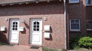 A two-story brick building with a tiled roof, two white doors, and a small window on the upper floor. - High-quality and bright: The upstairs apartment offers the fine and sat (Carolinensiel)