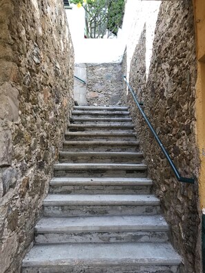 Un escalier étroit en pierre, doté de rampes métalliques, qui monte à travers un espace exigu aux murs rugueux.