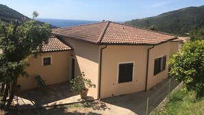 Um edifício térreo com telhado de cerâmica, um pequeno alpendre e vista para o mar.