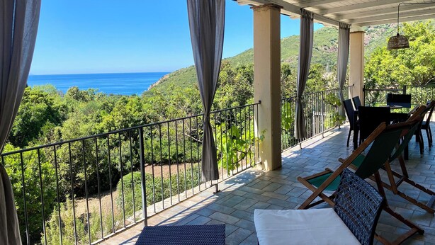 Uma área de estar coberta ao ar livre, com vista para o mar e vegetação.