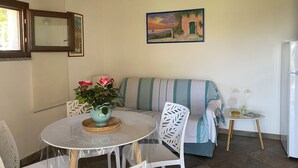 Uma sala de jantar com uma mesa redonda, cadeiras, um vaso com flores, um sofá listrado e um quadro na parede.