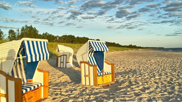 Zwei Liegestühle mit gestreifter Auflage an einem Sandstrand.