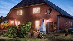 Ein zweistöckiges Ziegelhaus mit geneigtem Dach, Schornstein und einer gut beleuchteten Veranda mit Sitzgelegenheiten.
