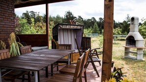 Eine Terrasse im Freien mit einem Holztisch und Stühlen, einer überdachten Sitzgelegenheit und einem steinernen Außenofen.