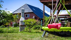 Ein Haus mit schrägem Dach, einem Schornstein und einem Garten mit Gras und kleinen Pflanzen.