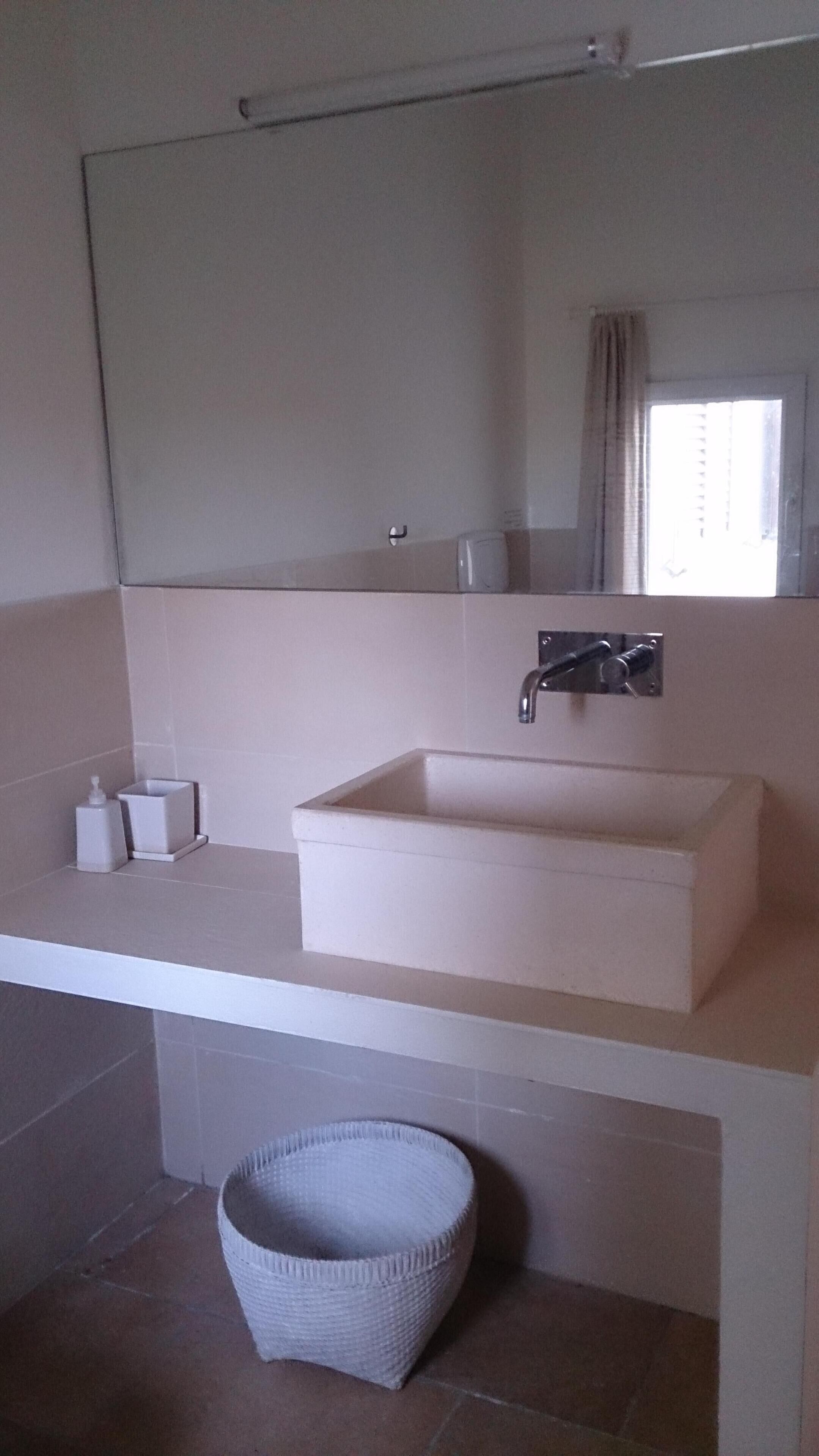 A bathroom with a white sink, a mirror above it, and a white basket on the floor.