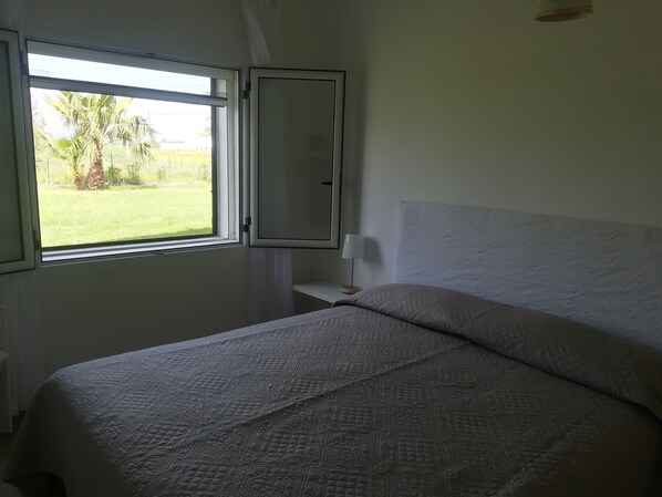 Een slaapkamer met een bed, een raam en een nachtkastje.