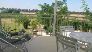 A balcony with a table and chairs, overlooking a green landscape with trees and a field.