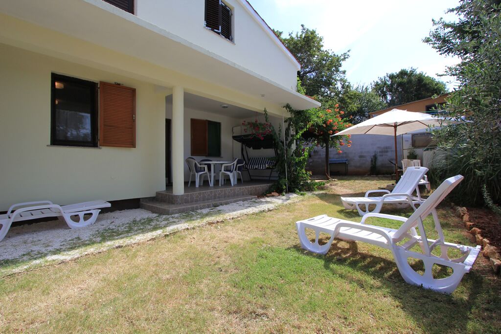 A white building with a covered patio area, outdoor seating, and a garden.