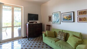A living room with a green sofa, a television, and artwork on the wall. - My Rental Homes - Il Giardino di Ravello with ample private garden and sea view (Ravello)