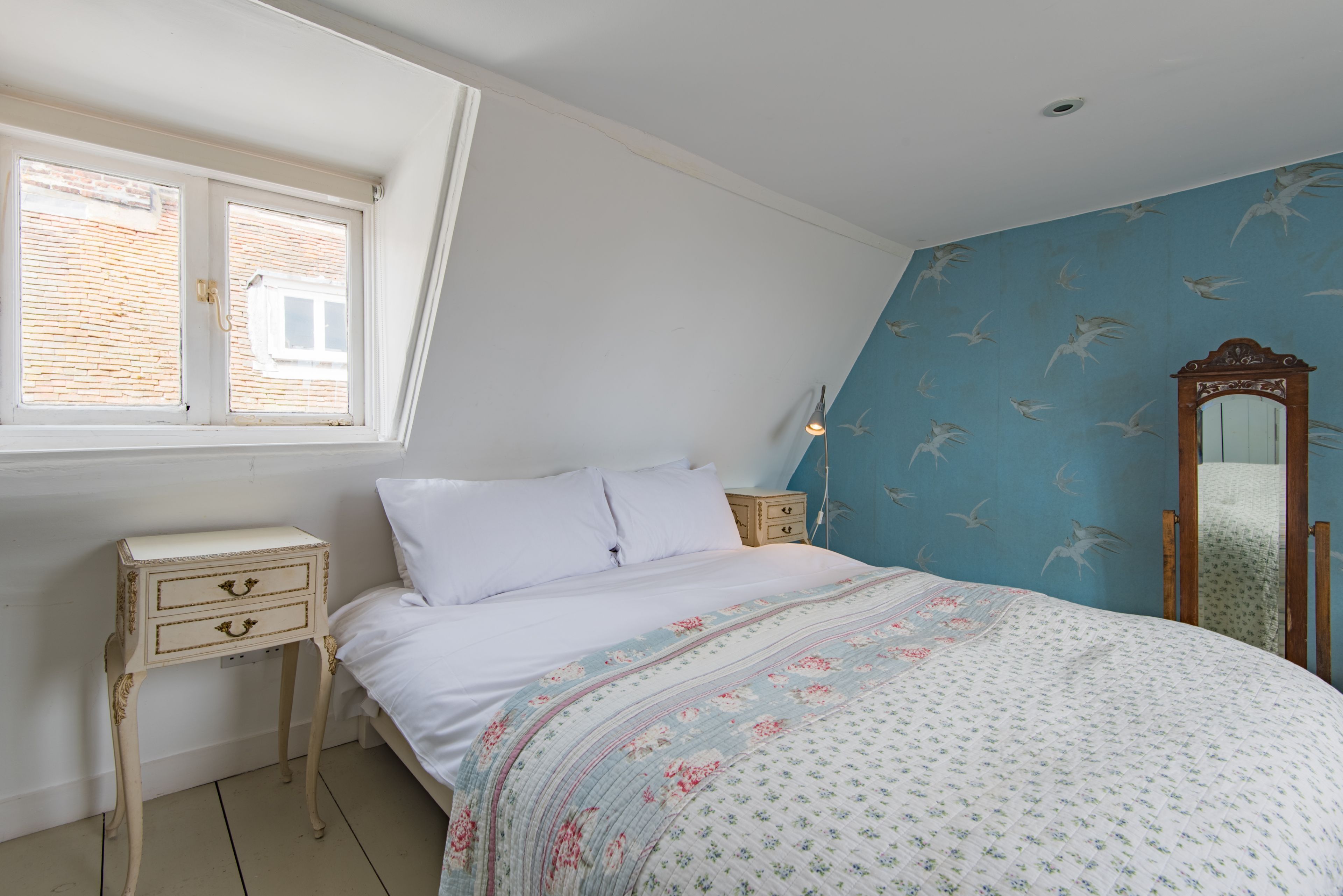 A bedroom with a bed, a nightstand, a dresser, a window, and a mirror.