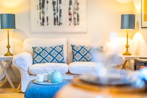 A cozy living room with a white sofa, patterned cushions, a blue teapot, and two lamps.