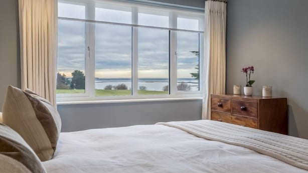 A bedroom with a large window, a bed, and a wooden dresser with decorative items. - River View, Aldeburgh (Aldeburgh)