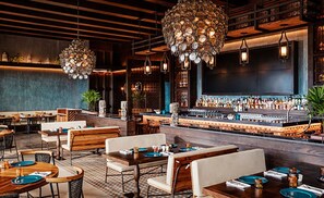 Een restaurant met houten tafels en stoelen, een bar met flessen en hangende lampen.