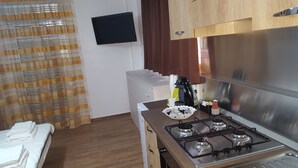 A compact kitchen with a gas stove, a small refrigerator, and a flat-screen TV mounted on the wall. - semi-detached holiday home center (Reggio Calabria)