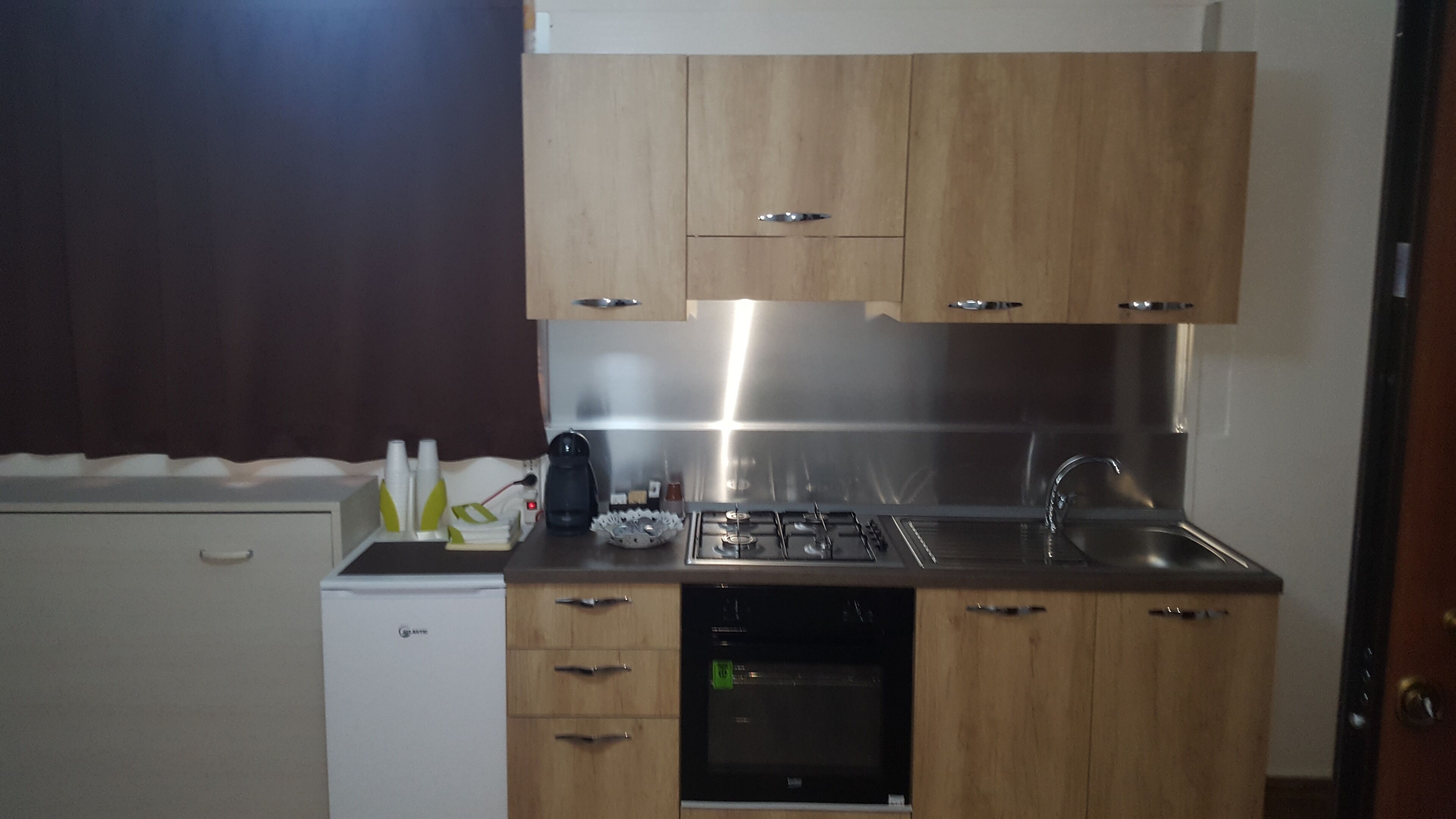 A compact kitchen with wooden cabinets, a built-in oven, and a stainless steel sink.