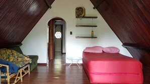 Una habitación en el ático con techo inclinado, suelo de madera, un sofá rojo, una mesa pequeña y un tapiz decorativo.